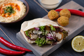 Falafel in pita with lettuce, blue onion and tahini sauce. Vegetarian shawarma on a wooden table with ingredients and hummus. Delicious and hearty lunch.
