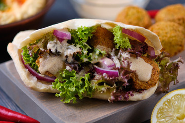 Falafel in pita with lettuce, blue onion and tahini sauce. Vegetarian shawarma on a wooden table with ingredients and hummus. Delicious and hearty lunch.