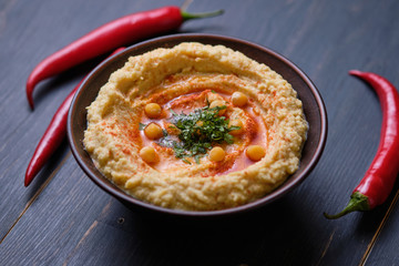 Classic hummus with hot pepper in a clay plate on a wooden table. National, vegetarian dish. General form.