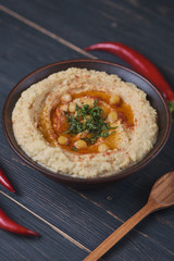 Classic hummus with hot pepper in a clay plate on a wooden table. National, vegetarian dish. General form.