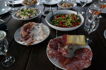 Mediterranean antipasti like salami and ham on a laid table with fresh salads for a rustic garden dinner - Powered by Adobe