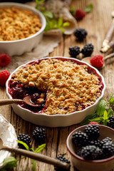 Crumble, Mixed berry (blackberry, raspberry) crumble, stewed fruits topped with crumble of oatmeal, almond flour, butter and sugar  in a baking dish on a wooden table, close-up