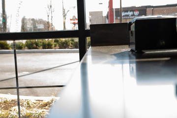 Close up of sunlight shining into dimly lit restaurant counter with napkin dispenser and view of fast food restaurant outside.