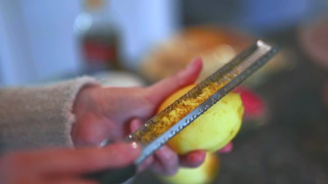 Female home cook zesting a freshly picked organic lemon in the kitchen.