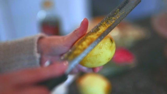 Female home cook zesting a freshly picked organic lemon in the kitchen.