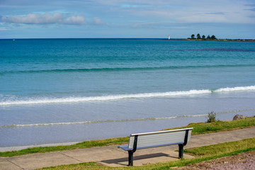 View of the ocean at Port Fairy with lighthouse in the background and empty bench seat in the foreground, Port Fairy Victoria Australia
