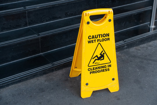 Bright Yellow Warning Janitorial Sign Of 'caution Wet Floor, Cleaning In Progress' At Front Of Wet Stairs To Warn Passersby For Safety.