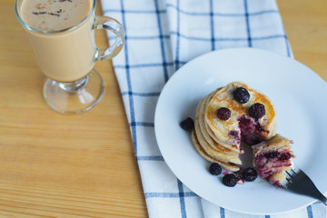 eating of fritter or pancakes with blackberry with fork on white dish and coffee on table with napkin, russian rustic breakfast, closeup view from above of horizontal lifestyle stock photo image