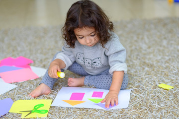 Cute little girl make applique, glues colorful house, applying a color paper using glue stick while doing arts and crafts in preschool or home. The idea for children's creativity, art project.