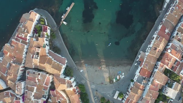 Straight down drone view of turquoise water of bay, beach, seaside promenade and white houses with tiled roofs on it, narrow streets of coastal spanish town Cadaques