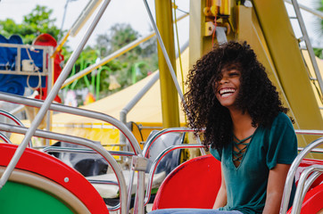 young girl of black color, laughing hair in ferris wheel, sitting enjoying a summer day, lifestyle portrait