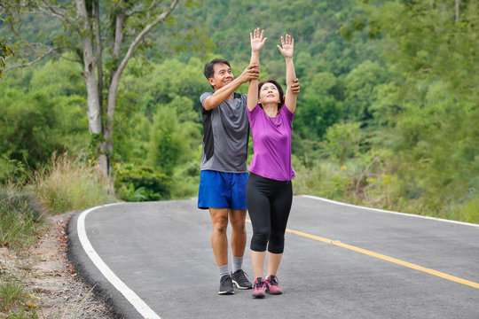 Asian Middle Aged Couple Stretching Muscles Before Jogging In Park