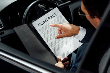 cropped view of african american businessman in suit reading contract in car at sunny day