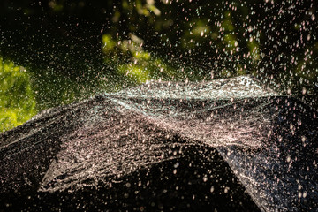 close up black umbrella with splashes and raindrops during heavy rain outdoor