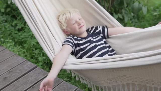Happy boy blond sleeps in hammock in summer at the cottage. Slow motion