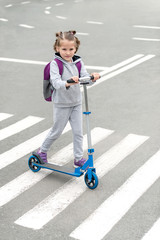 Schoolgirl carrying scooter and crossing road on way to school. Zebra traffic walk way in the city....