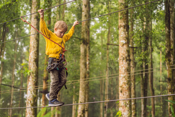 Naklejka na ściany i meble Little boy in a rope park. Active physical recreation of the child in the fresh air in the park. Training for children