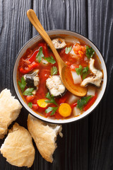 Eel soup with tomatoes, potatoes, carrots, onions, peppers and herbs closeup in a bowl. Vertical top view
