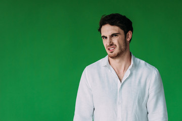 disgusted man in white shirt looking at camera isolated on green