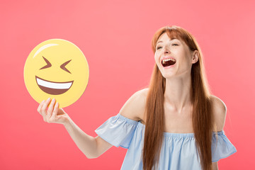 excited redhead girl holding laughing smiley isolated on pink