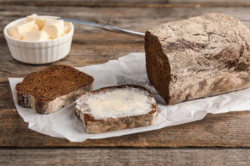 Slice of rye bread with butter near loaf on wooden table