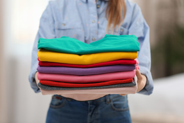 Woman holding folded clean clothes indoors, closeup. Laundry day