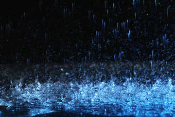 Heavy rain falling down on ground against dark background, toned in blue