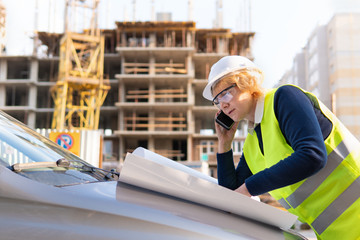 Builder woman at construction site in vest and helmet with the drawing paper