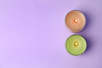 Burning wax candles in glass holders on purple background, flat lay. Space for text