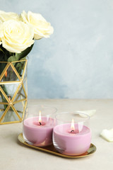 Burning candles in glass holders and roses on light table, space for text