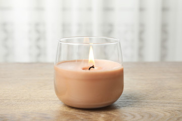 Burning candle in glass holder on wooden table