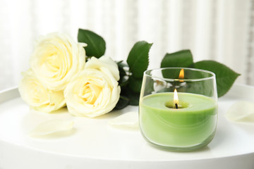 Burning candle in glass holder and roses on white table, space for text
