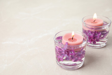 Obraz na płótnie Canvas Glass holders with water, lilac flowers and burning candles on light table, space for text