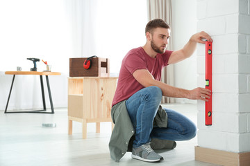 Young working man using construction level at home, space for text - Powered by Adobe