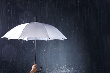 Woman holding white umbrella under rain on dark background, closeup