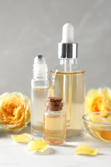 Bottles and bowl of rose essential oil and fresh flowers on white table