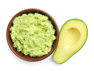 Bowl of tasty guacamole and cut avocado on white background, top view