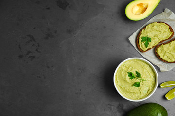 Flat lay composition with bowl of guacamole made of ripe avocados on grey table. Space for text