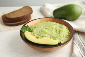 Bowl with guacamole made of ripe avocados served on white wooden table