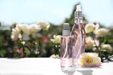 Bottles of facial toner with essential oil and fresh rose on table against blurred background. Space for text