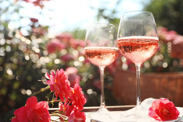 Glasses of rose wine on table in blooming garden