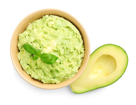 Bowl Of Tasty Guacamole With Basil And Cut Avocado On White Background, Top View