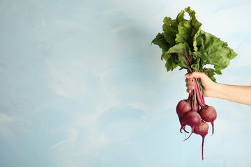 Young woman holding bunch of fresh beets on blue background, closeup. Space for text