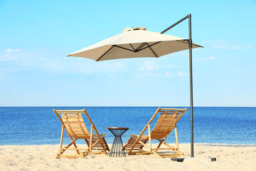 Empty wooden sunbeds and beach accessories on sandy shore