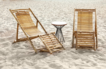 Empty wooden sunbeds and table on sandy shore. Beach accessories