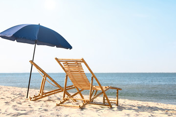 Empty wooden sunbeds and umbrella on sandy shore. Beach accessories