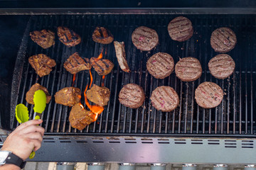 overhead high angle view of summer BBQ on a propane gas grill beef hamburger, lamb chops and man...