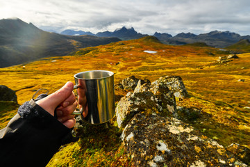 Man holding a cup of coffee with golden landscapes in the background on Lofoten Islands