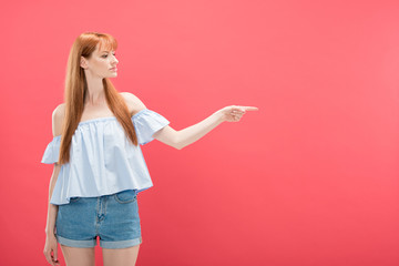 redhead woman in denim shorts pointing with finger isolated on pink