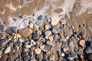 nature background image of beach with pebble stones and wave foam. view from above